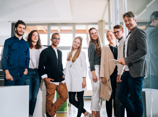 Group of eight people standing together and smiling in an office setting