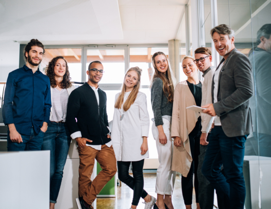 Group of eight people standing together and smiling in an office setting