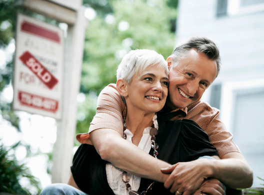 happy older couple sitting in front of sold house
