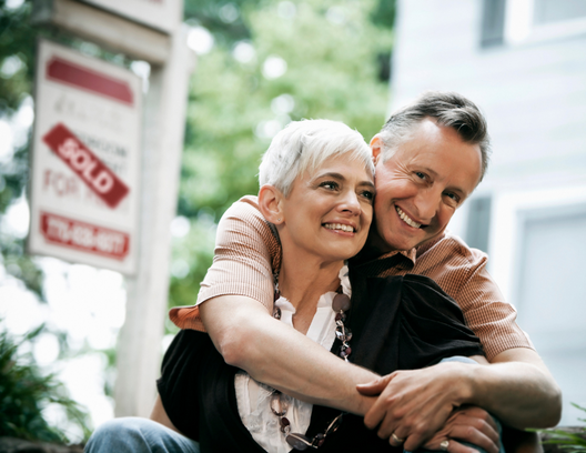 happy older couple sitting in front of sold house