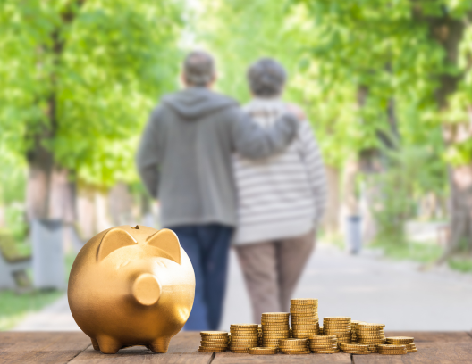 An older couple walking together in the distance and a piggy bank and stacks of coins in front.
