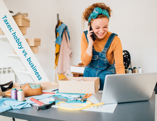 A young woman on phone in a work room at a computer surrounded by fabric and materials to make crafts.